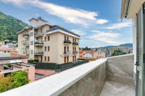 Vista dal balcone sullo skyline di Como con moderni edifici residenziali e verdi colline presso Lago Suites