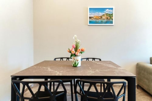 Zona pranzo dell'appartamento Lago Suites Como con tavolo, sedie nere, fiori e opere d'arte costiera