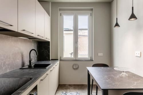 Cucina e zona pranzo moderne in appartamento Lago Suites Como con banconi in marmo scuro, mobili bianchi e vista sulla città