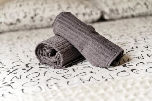 Asciugamani grigi arrotolati ordinatamente su biancheria da letto fantasia presso l'appartamento Lago Suites Como