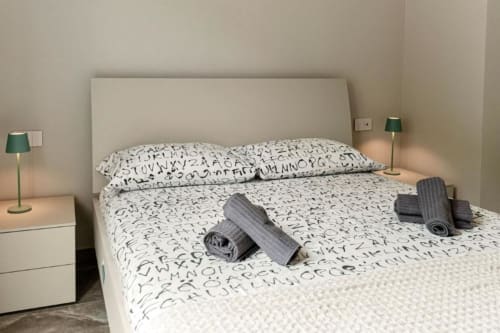Camera moderna di Lago Suites Como con biancheria a motivo alfabetico, asciugamani grigi, lampade verdi e testata beige