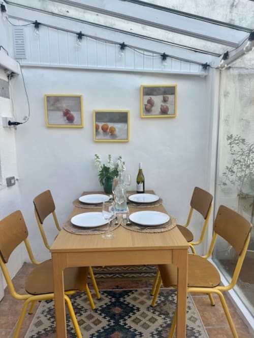 Bright dining area at 2 Doves Holiday Property with wooden table, yellow chairs, and fruit artwork on white walls.
