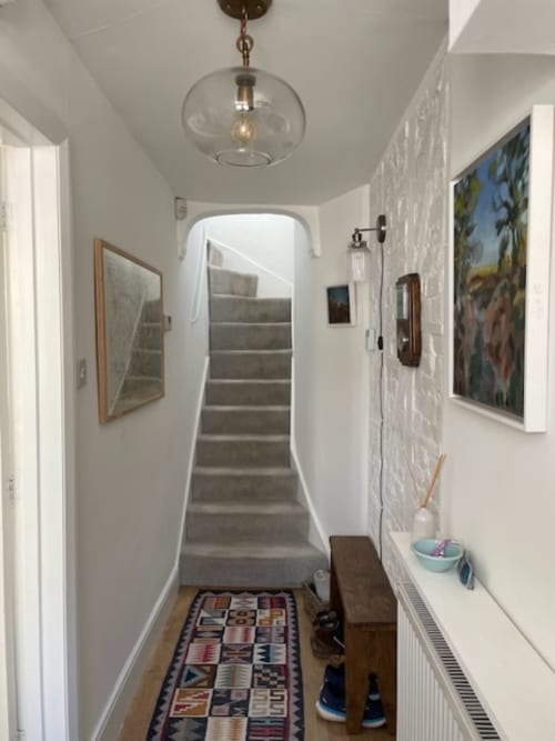 Narrow hallway at 2 Doves Holiday Property in Topsham with stairs, pendant light, framed artwork, and geometric patterned