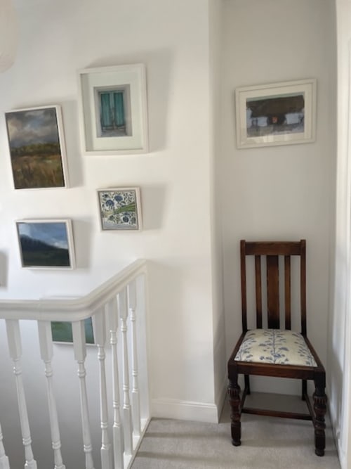 Hallway at 2 Doves Holiday Property featuring white staircase railing, framed artwork on walls, and antique wooden chair with