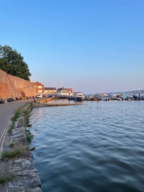Topsham riverside harbor with moored boats, brick buildings, and waterfront promenade on a clear day