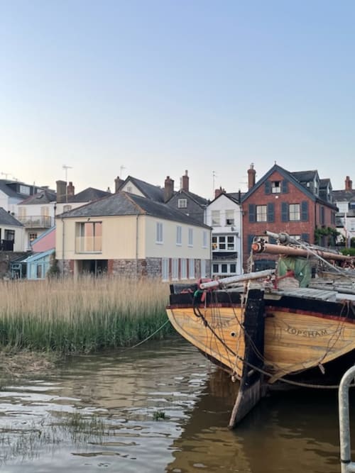 Wooden boat moored at Topsham waterfront with historic riverside buildings and marsh grasses, Exeter
