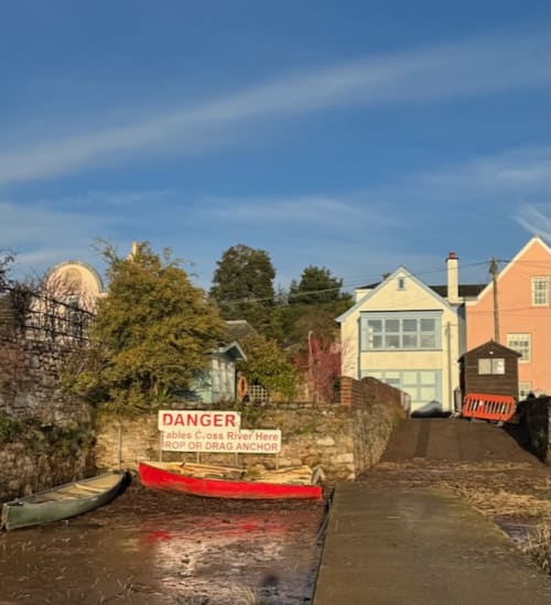 Waterfront cottages in Topsham, Exeter with moored boats and danger sign at river crossing