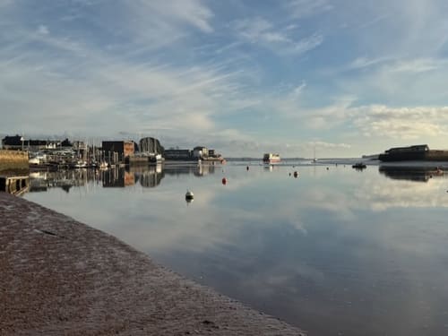 Topsham waterfront with calm harbor, boats, and historic buildings reflecting in still water