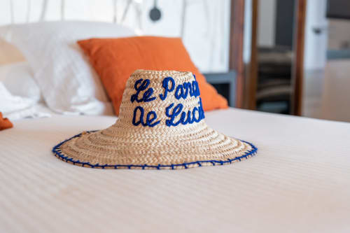 Chapeau de paille avec broderie bleue « Le Paradis de Lucile » posé sur un lit à la maison d'hôtes de Giverny
