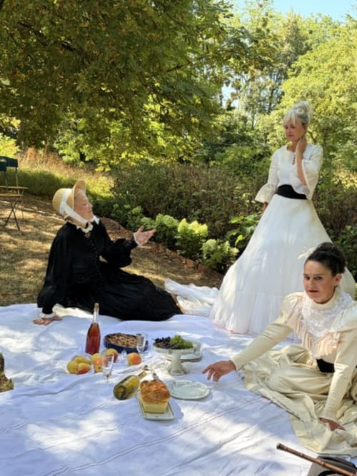 Three women in period costume enjoying a picnic lunch outdoors at Domaine de l'Ocrerie in Pourrain, France