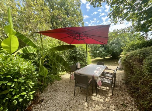 Red umbrella shading outdoor dining table in lush garden at Gîte La Vieille Ferme, Saint-Geniès