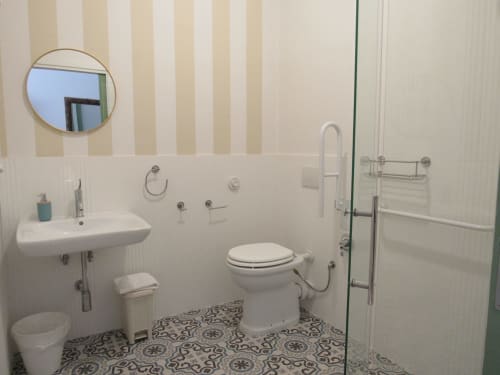 Bagno accessibile moderno presso l'Il 900 B&B ad Avezzano con doccia, wc, lavabo, specchio rotondo e pavimento con piastrelle decorate