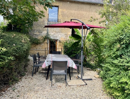 Área de comedor al aire libre en Gîte La Vieille Ferme con sombrilla roja, mesa y sillas en un patio ajardinado