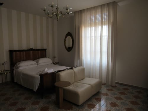 Elegante camera da letto all'Il 900 B&B di Avezzano con letto in legno scuro, biancheria color crema, carta da parati rigata e vista sulla città
