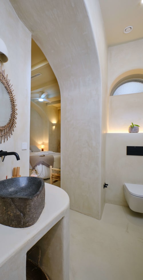Modern bathroom with curved stone partition, dark vessel sink, and ensuite bedroom access at EntreArcos Casa Eco-Boutique in