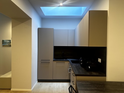 Cucina moderna nella suite Lago Suites Como 001 con armadiatura grigia, piano nero, lucernario e TV a schermo piatto