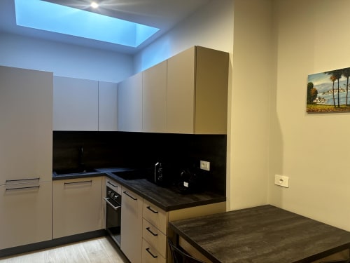 Moderna cucina di Lago Suites Como con mobili beige, piano di lavoro nero, elettrodomestici incassati e lucernario.
