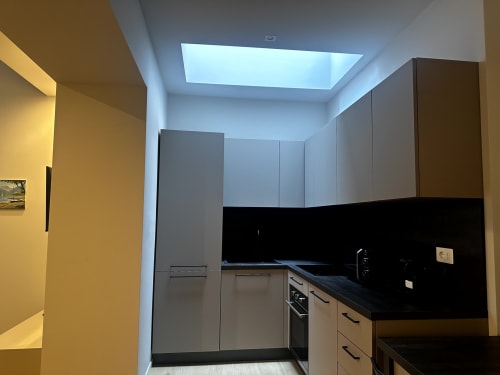 Cucina moderna a Lago Suites Como con piano di lavoro nero, mobili grigio, lucernario e parete gialla