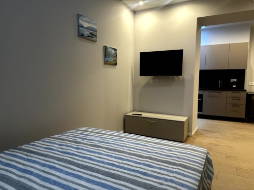 Camera 001 Lago Suites Como: letto con biancheria a righe, TV a schermo piatto a parete, angolo cucina e arredi moderni