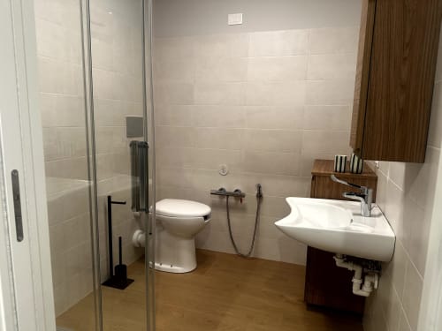 Bagno accessibile a Lago Suites Como con doccia walk-in, lavabo bianco, wc e pavimento in legno