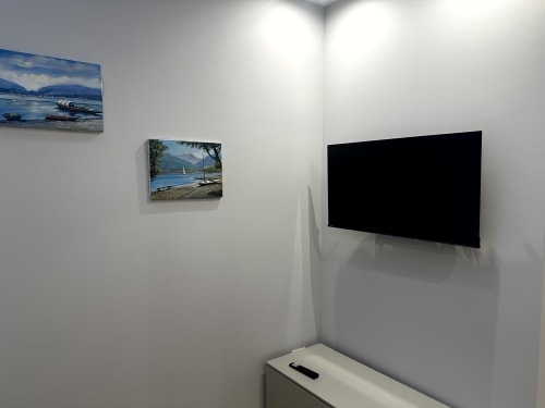Angolo della moderna camera d'hotel presso Lago Suites Como con TV a schermo piatto e quadri paesaggistici con barche e vedute del lago su sfondo bianco
