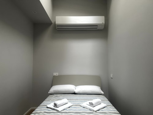 Camera minimalista presso Lago Suites Como con unità split, biancheria a righe, cuscini bianchi e asciugamani arrotolati