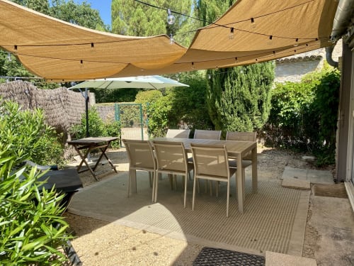 Private garden patio at Le Mas de la Soie cottage with dining table, shade sails, and lush greenery in Entrechaux, France