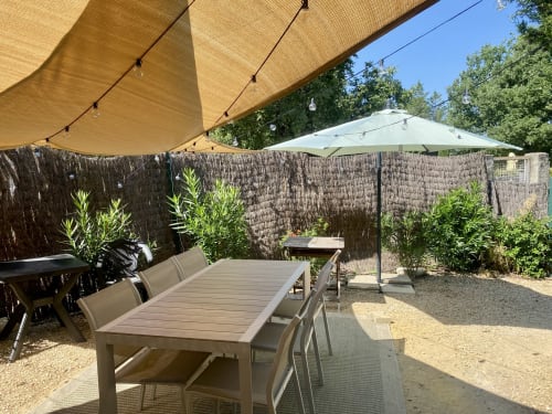 Private garden patio at Le Mas de la Soie cottage with dining table, shade sails, and green landscaping in Entrechaux