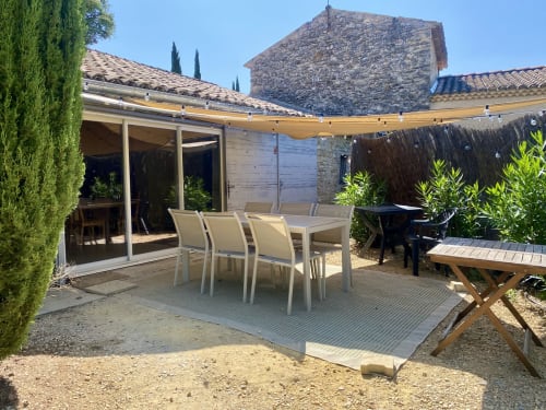 Sunny garden patio at Le Mas de la Soie cottage in Entrechaux with dining table, yellow awning, and stone buildings