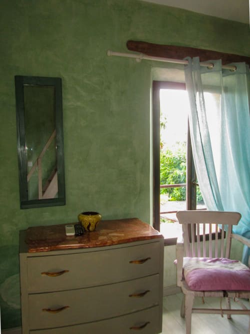 Camera da letto verde al Clos Bb a Saint-Cyr sur Mer con cassettone bianco, specchio, sedia e porte-finestre che si affacciano sul giardino
