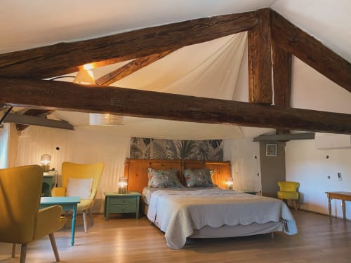 Chambre spacieuse du Mas de la Soie avec poutres en bois apparentes, fauteuils jaunes et vue sur le jardin à Violès