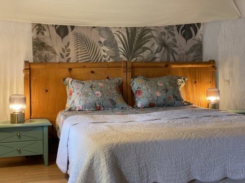 Chambre lumineuse au Mas de la Soie avec tête de lit en bois, oreillers fleuris et papier peint botanique à Violes, France