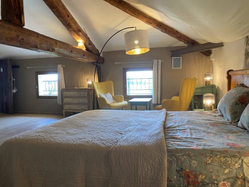 Chambre spacieuse au Mas de la Soie avec deux lits, poutres en bois, lampadaire arc, chaises jaunes et vue sur le jardin à Violès