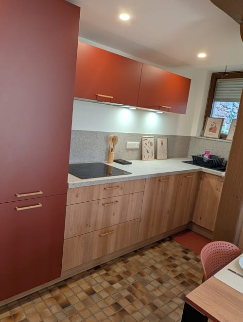 Cuisine moderne équipée aux murs rouges, meubles bas en bois et plan de travail gris du gîte Bi d'Tante Irène à Kirrwiller