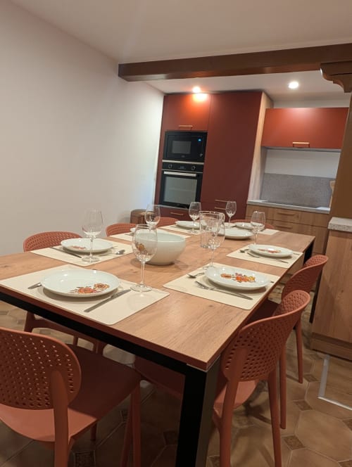 Salle à manger moderne du gîte Bi d'Grosseltere avec table en bois, chaises corail et cuisine équipée à Kirrwiller