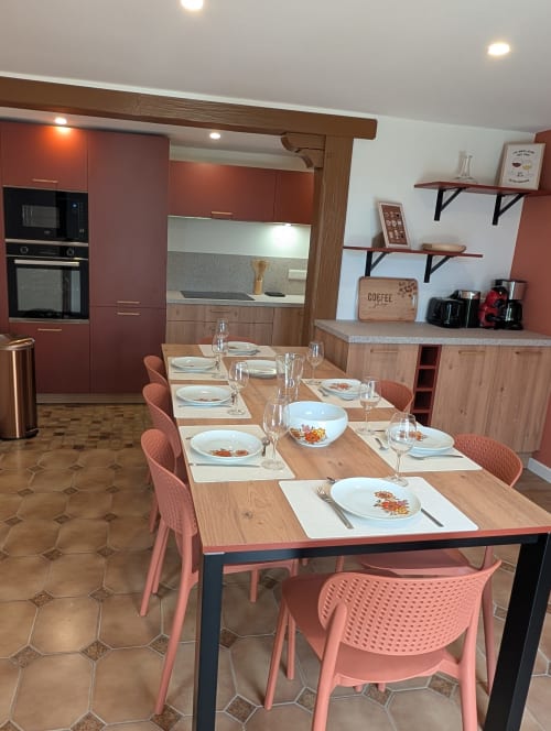 Salle à manger cottage moderne au Bi d'Grosseltere avec table dressée, chaises roses et cuisine équipée à Kirrwiller