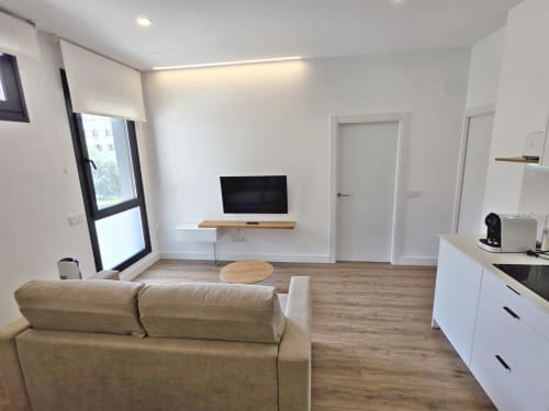 Moderna sala de estar en BR Silgar Sanxenxo con sofá beige, TV, cocina y suelo de madera