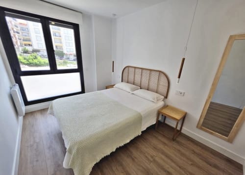 Dormitorio moderno en BR SILGAR Sanxenxo con cama queen, muebles de madera y gran ventanal con marco negro con vistas a la ciudad