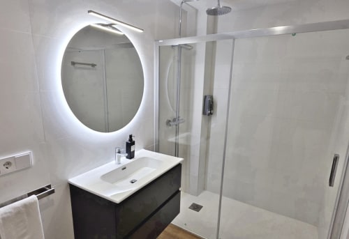 Baño moderno en BR Silgar Club, Sanxenxo con espejo redondo iluminado, tocador oscuro y ducha de obra con rainfall