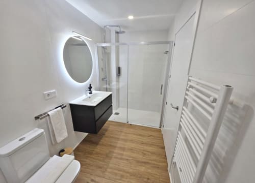 Baño moderno en habitación BR Silgar Club, Sanxenxo, con espejo iluminado, tocador negro, ducha a ras de suelo, inodoro y toallero calefactable