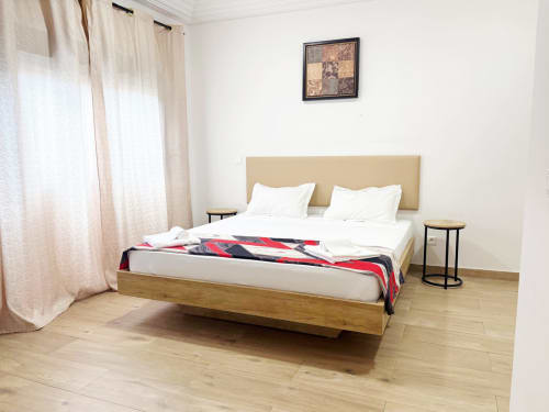 Dormitorio moderno con cama de madera, ropa de cama blanca y cabecero beige en el apartamento DakarByDays en Dakar, Senegal
