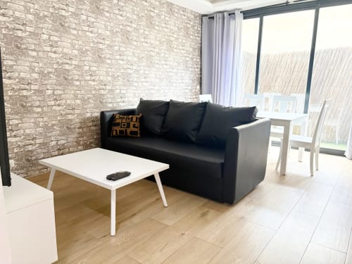 Sala moderna del apartamento EMMA DakarByDays con sofá negro, mesa de centro blanca, pared de ladrillo y balcón con vistas