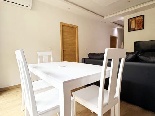 Comedor moderno en el Apartamento EMMA DBD901 de Dakar con mesa blanca, sillas y sofá negro