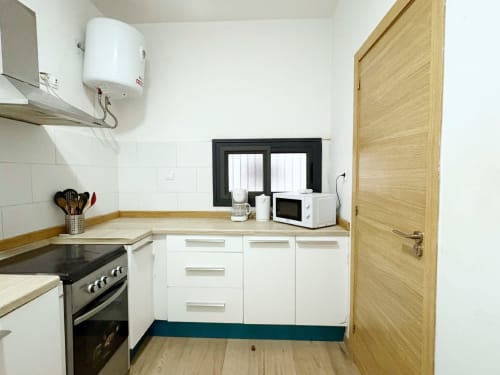 Cocina moderna en el Apartamento EMMA, Dakar con gabinetes blancos, estufa, microondas y puerta de madera