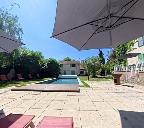 Terrasse piscine de la Maison Agami avec parasols, transats et dallage en pierre dominant la piscine rectangulaire à Rosières aux