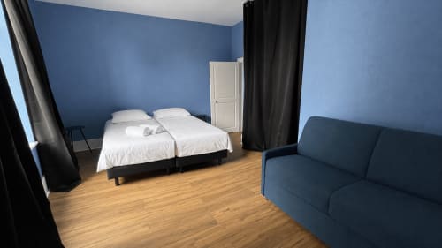 Chambre moderne à Maison Agami avec lits jumeaux, murs bleus, canapé et parquet à Rosières aux Salins