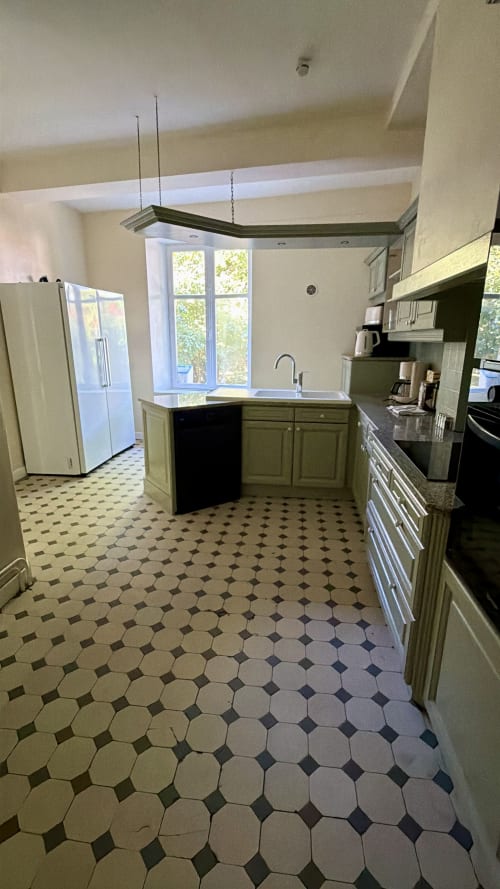 Cuisine spacieuse du gîte Maison Agami avec armoires vertes, îlot avec évier et carrelage noir et blanc