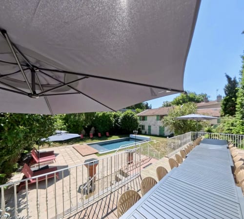 Vue de la piscine du gîte Maison Agami avec terrasse en bois, chaises longues et parasol blanc à Rosières aux salines