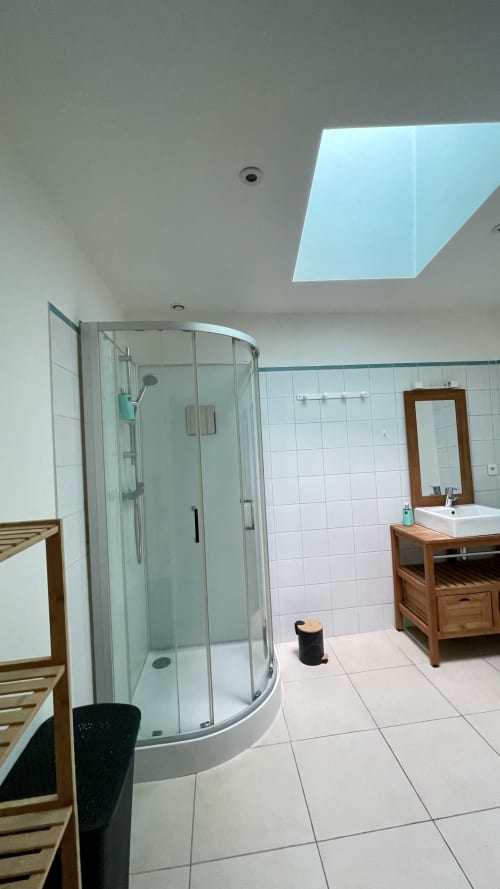 Salle de bain moderne avec puits de lumière à la villa Maison Agami, douche en verre courbe et meuble vasque en bois