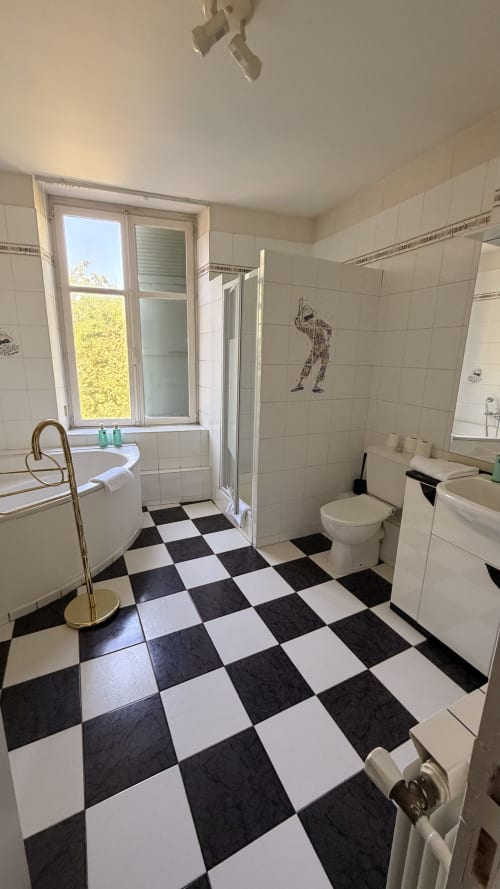Salle de bain spacieuse de la villa Maison Agami avec carrelage damier noir et blanc, baignoire, douche et vue fenêtre